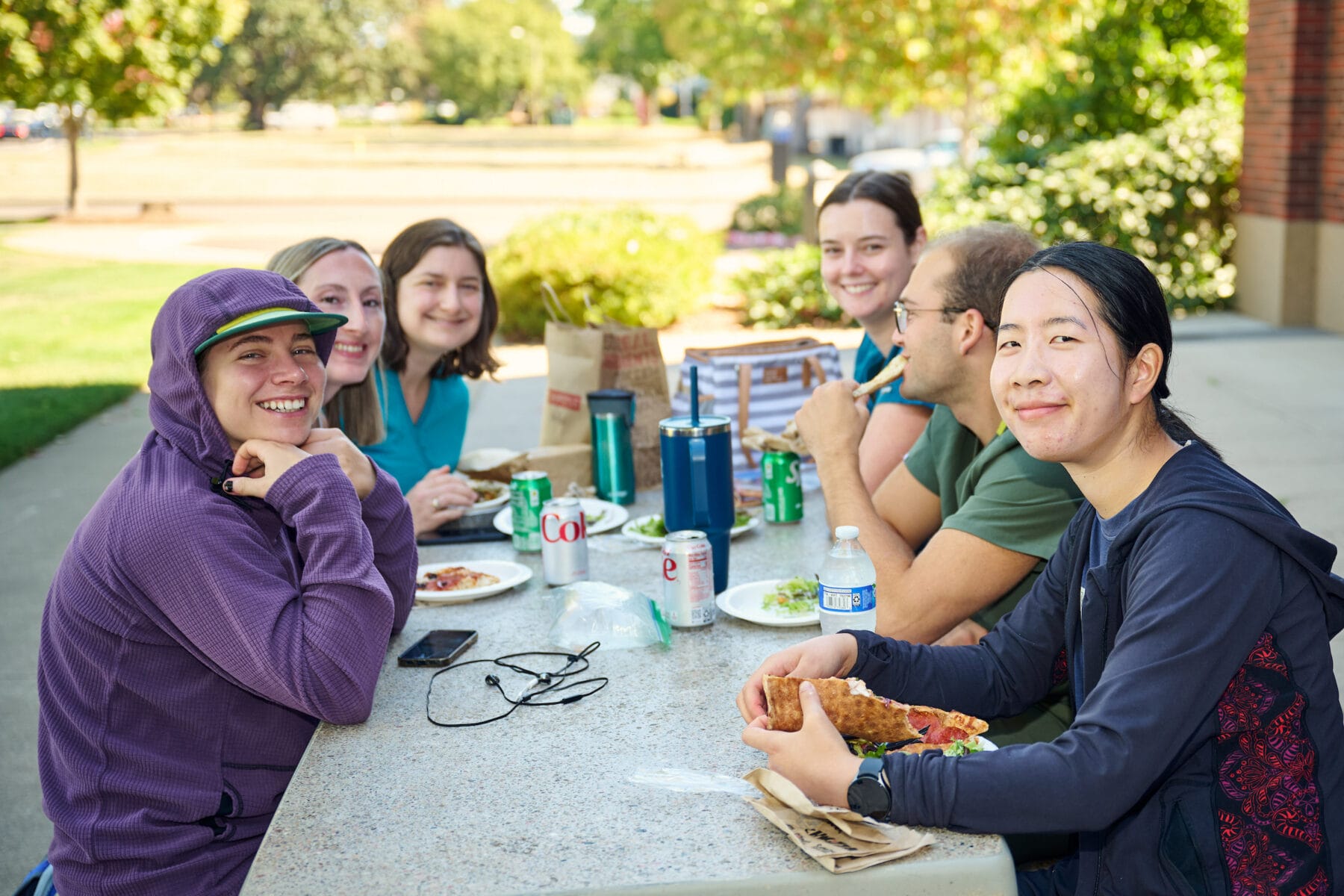 Six people at a picnic table eating pizza