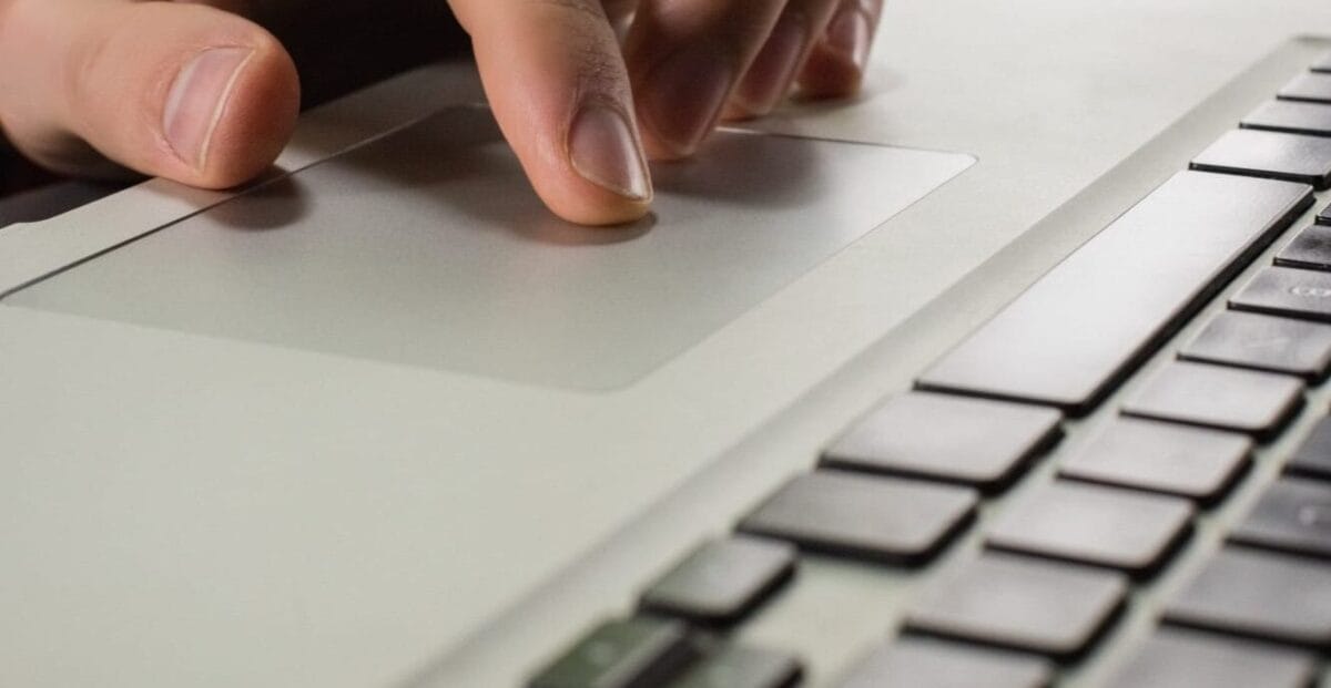 A hand uses the trackpad of a laptop, with part of the keyboard visible in the foreground.