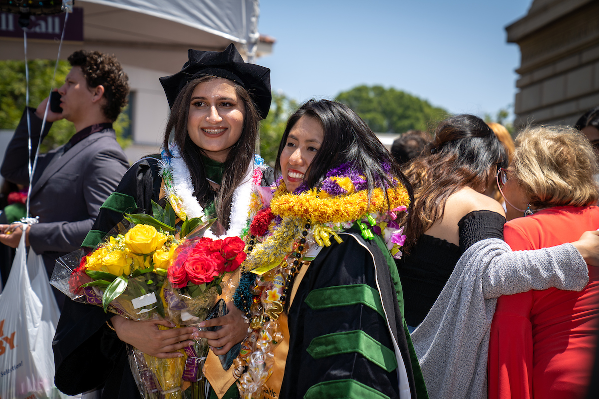 Two women in graduation robes with flowers in their hands.