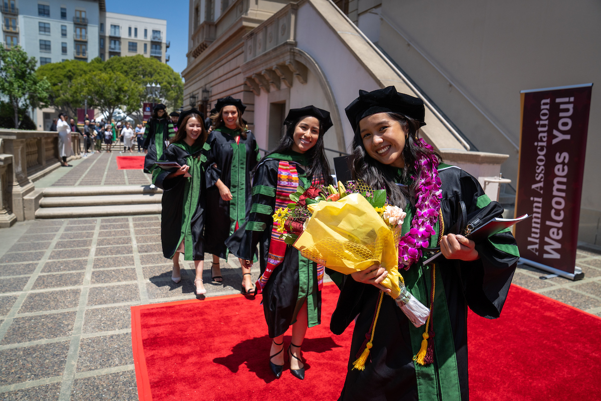 A group of women in graduation gowns walking down a red carpet.