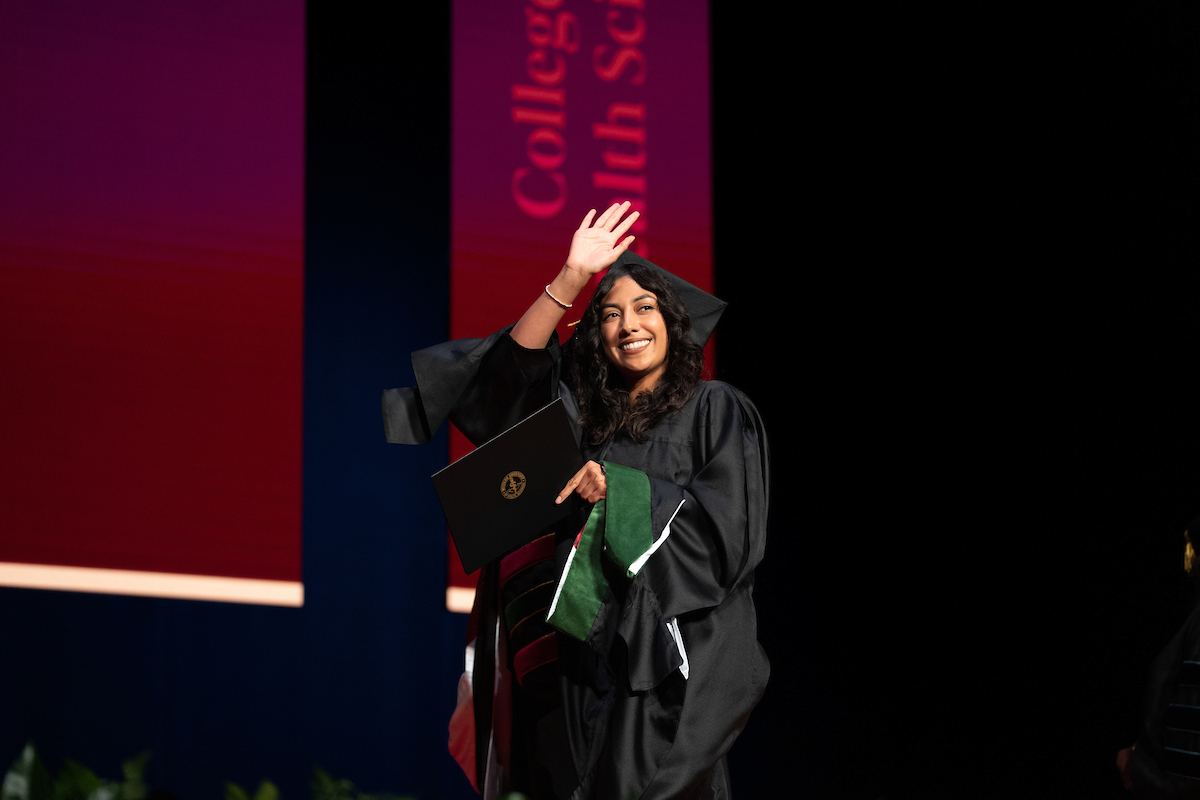 A woman in a graduation gown waves on stage.