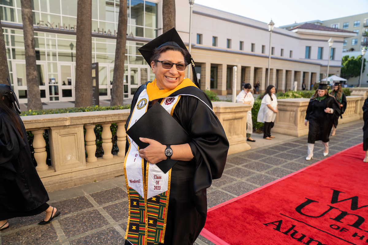 A man in a graduation gown standing on a red carpet.