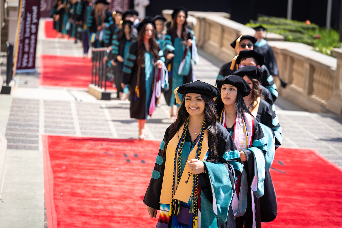 A group of women in graduation gowns walking down a red carpet.