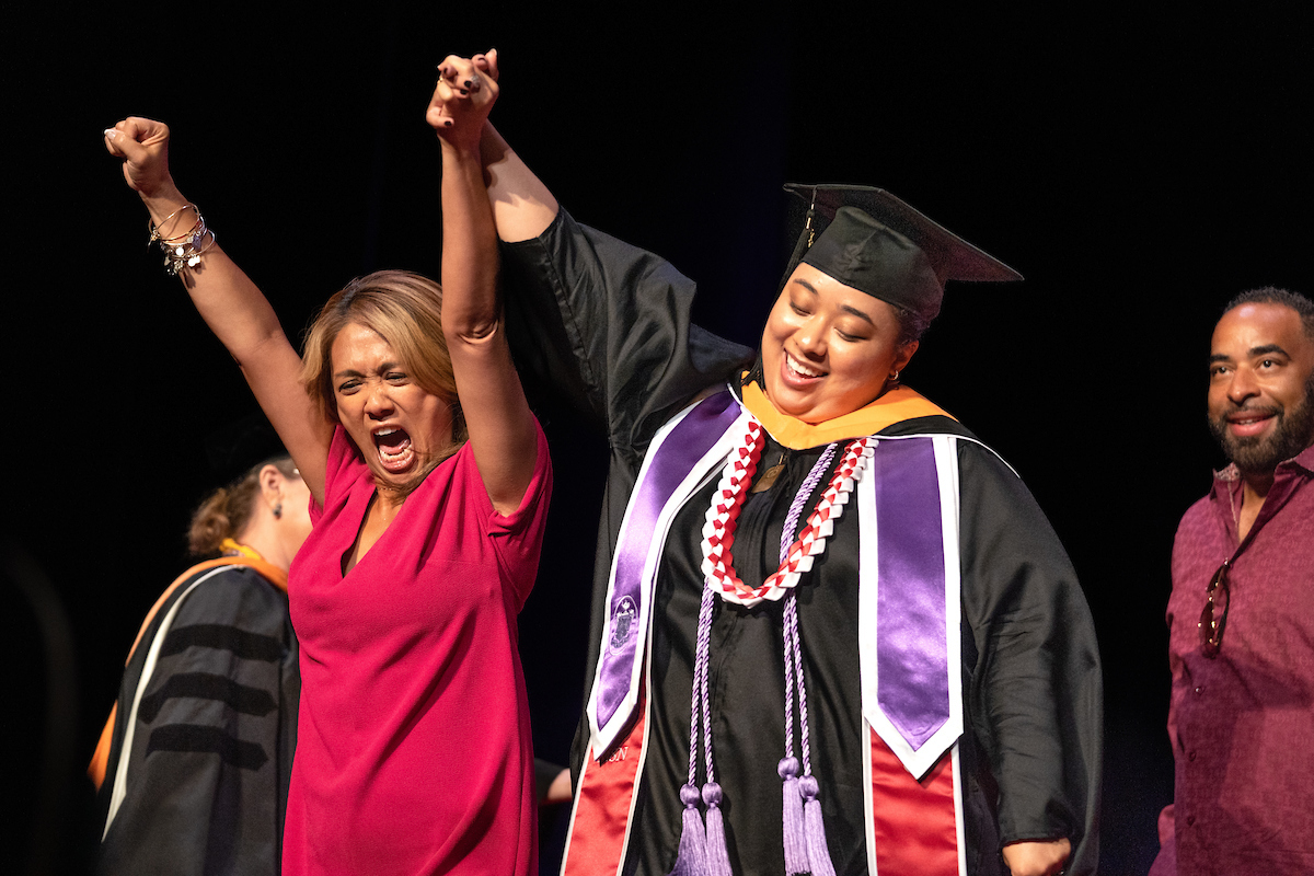 A woman in a graduation gown celebrates with her family.