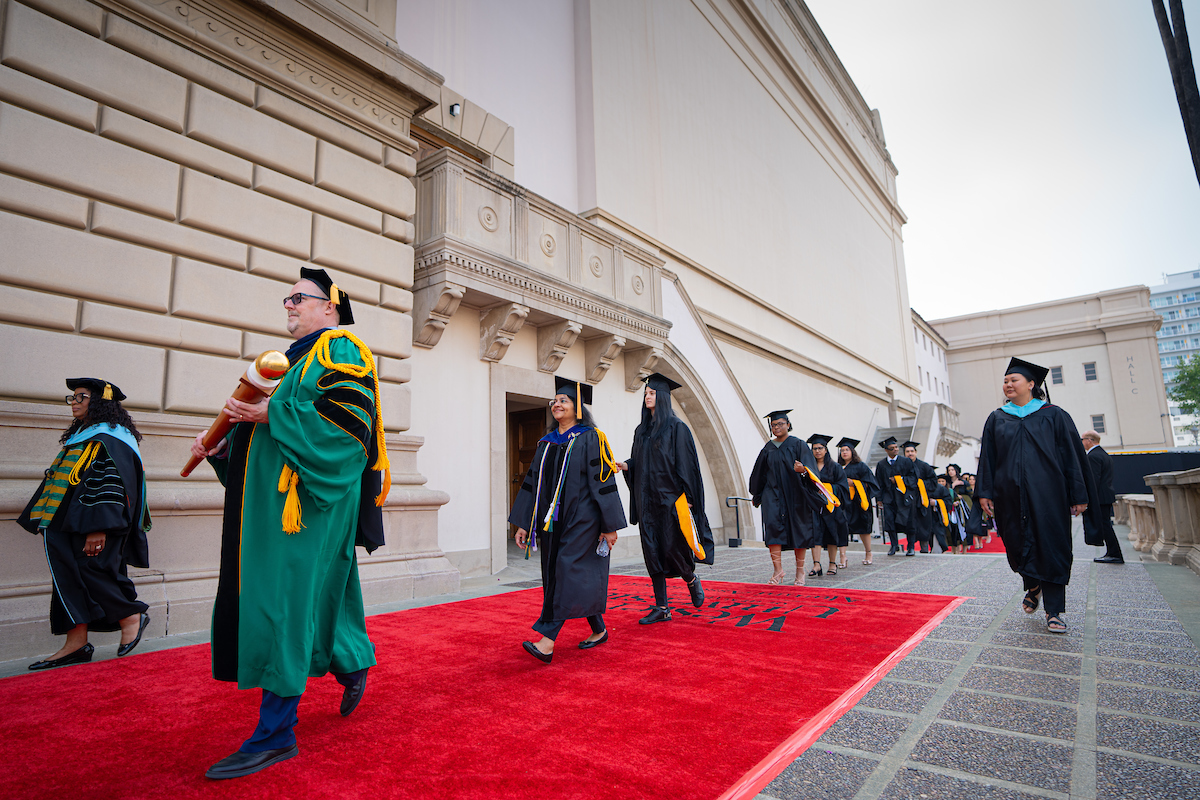 A group of graduates walking down a red carpet.