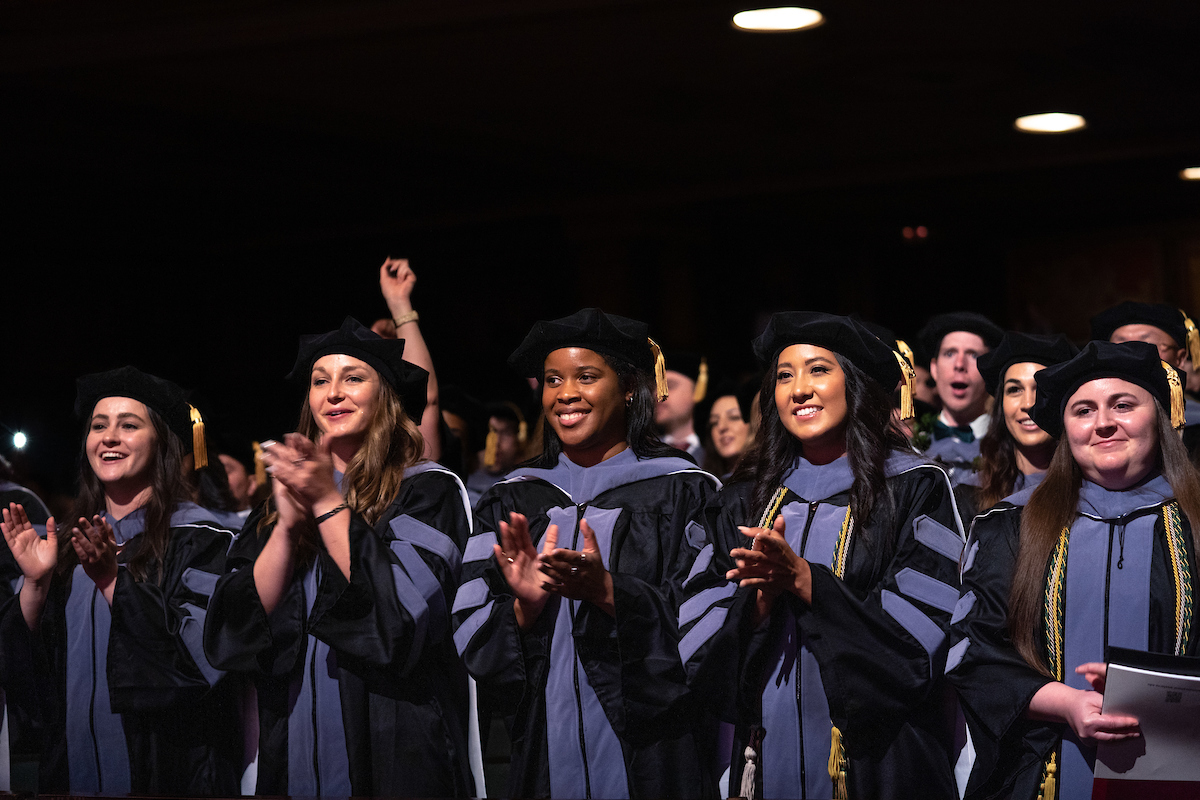 A group of graduates clapping at a graduation ceremony.