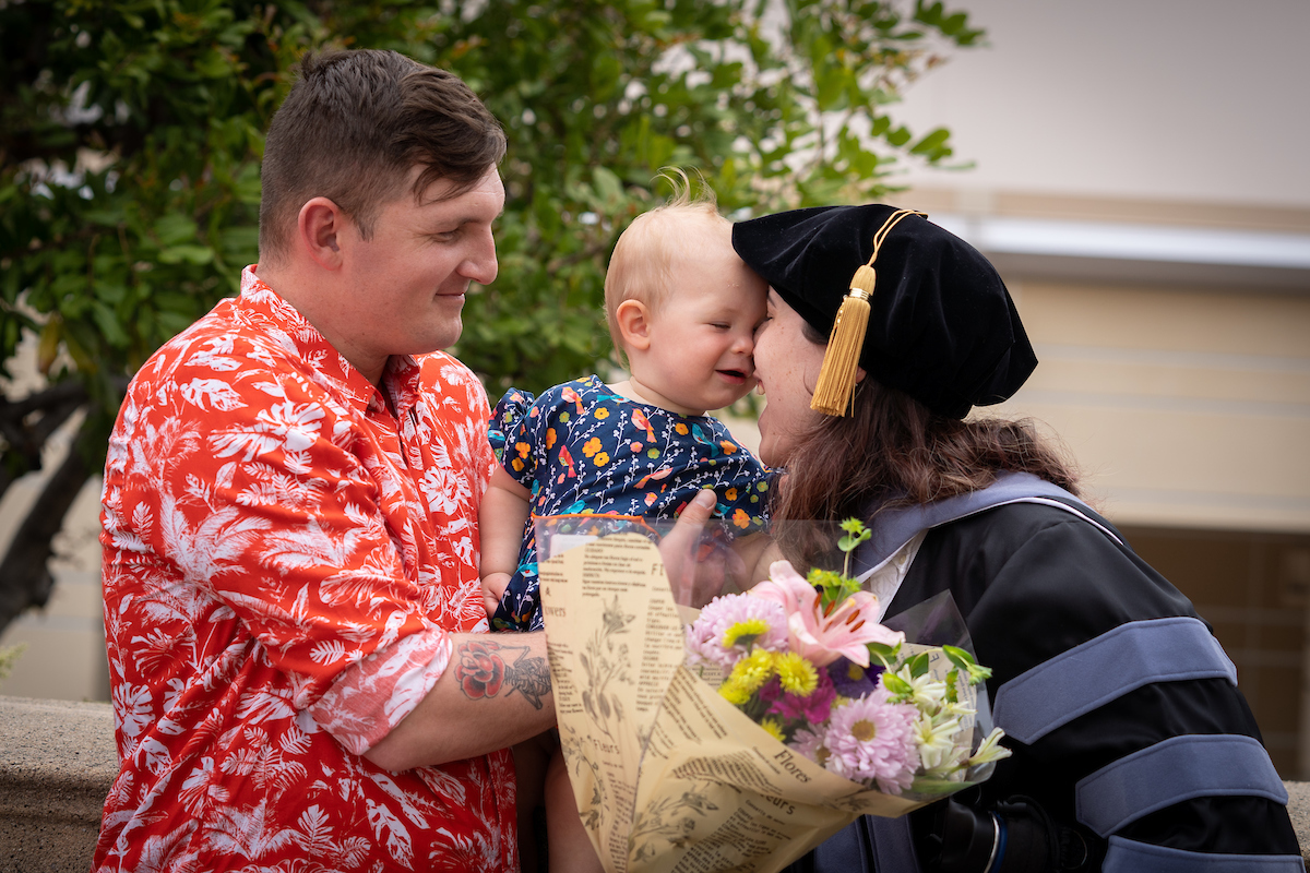 A woman in a graduation gown kisses a baby.