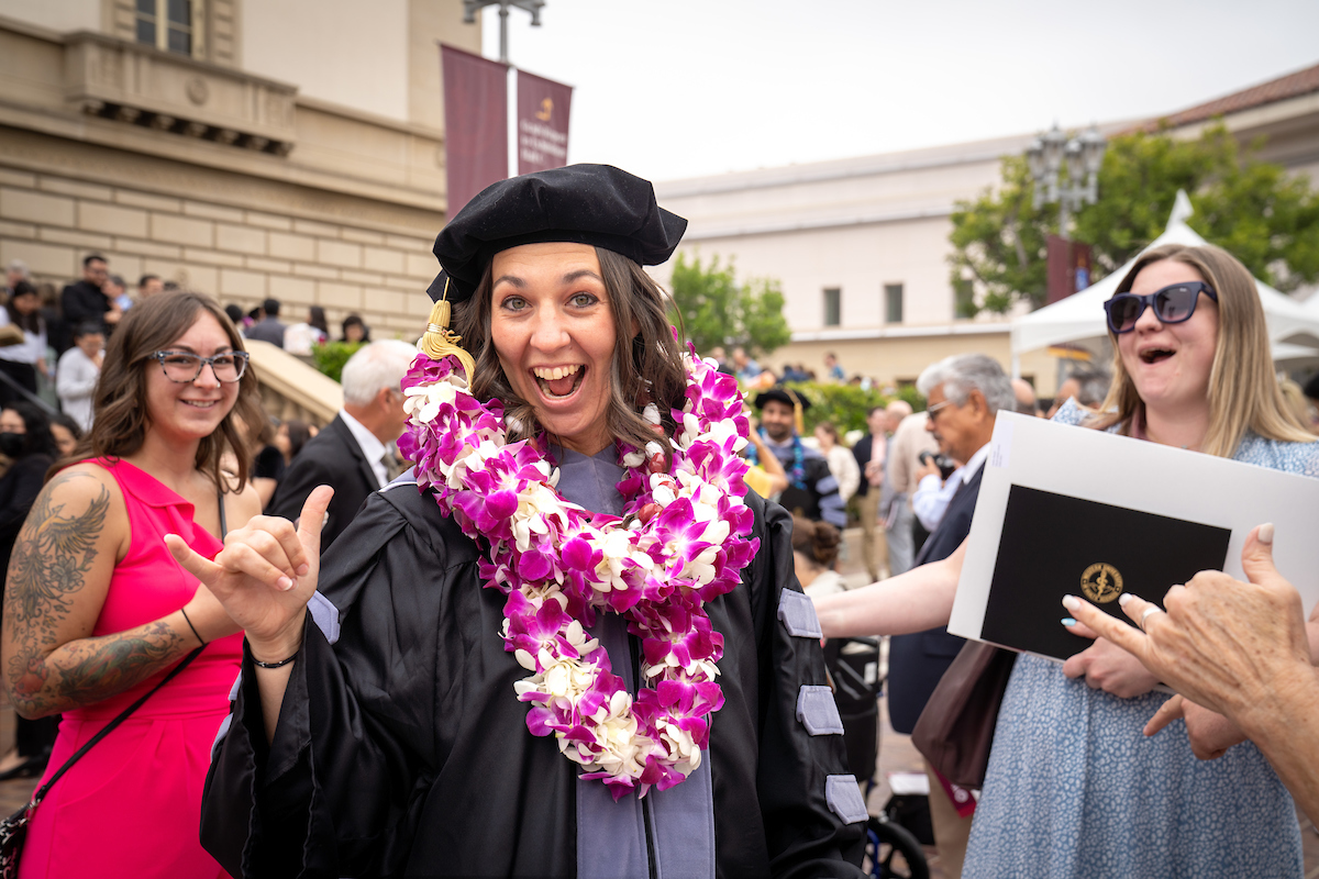 A woman in a graduation gown is smiling at the crowd.
