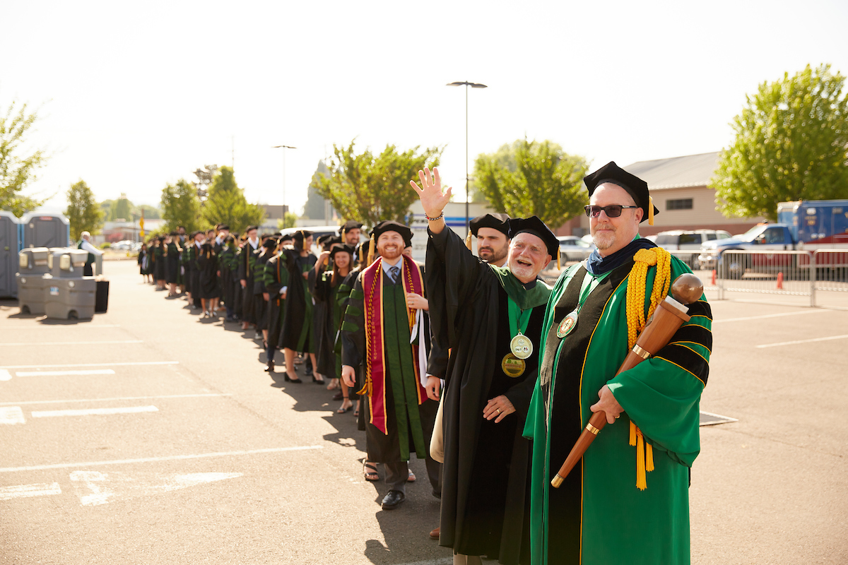A group of men in graduation robes standing in a parking lot.