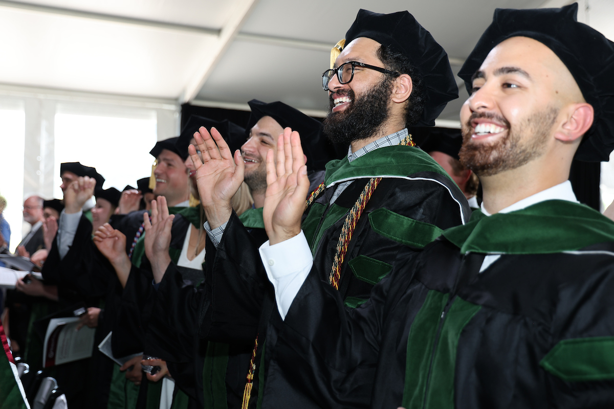 A group of men in graduation robes clapping.