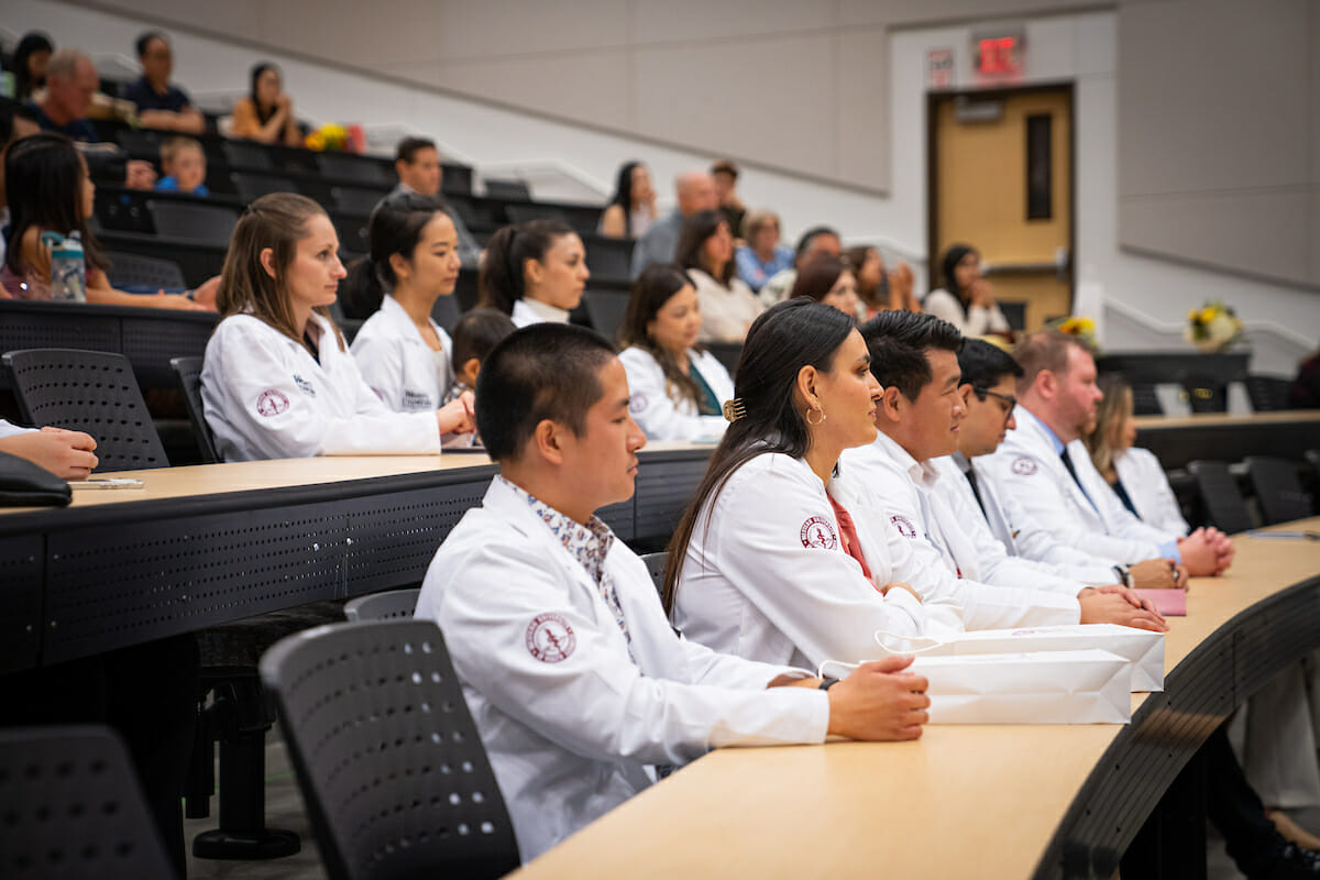 A group of people in white coats sitting in a lecture hall.
