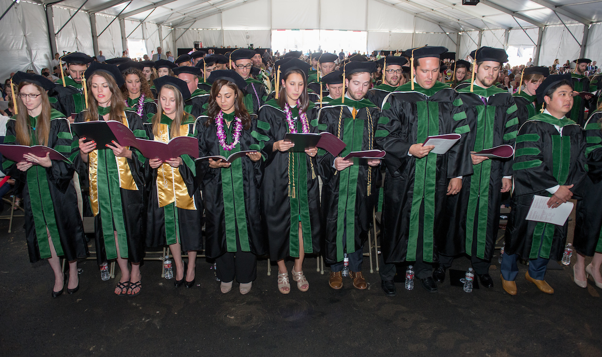 A group of people in graduation robes standing in a large auditorium.