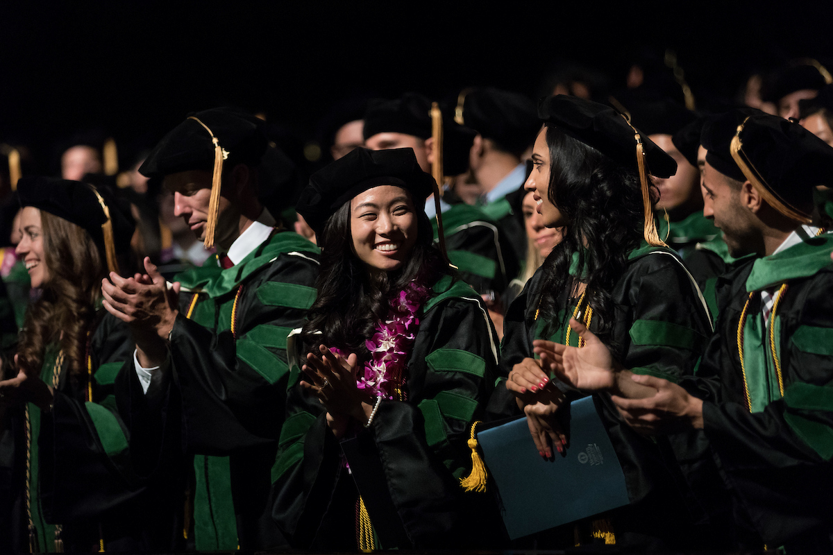 A group of graduates in green robes clapping.