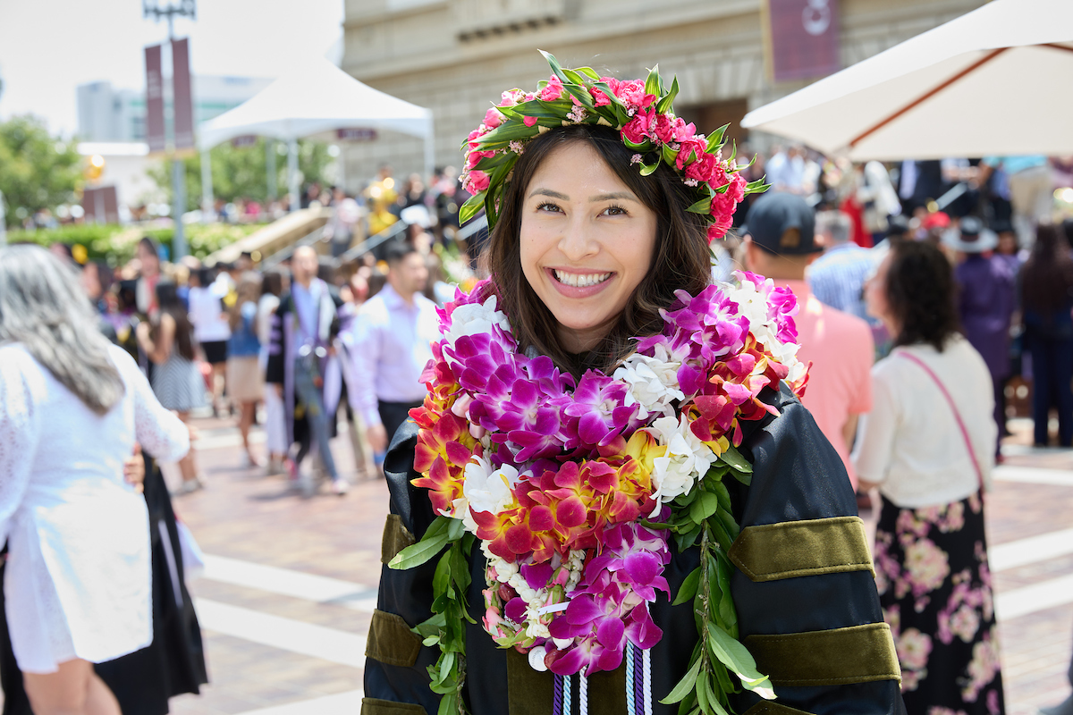 A woman in a graduation gown smiles in front of a crowd.
