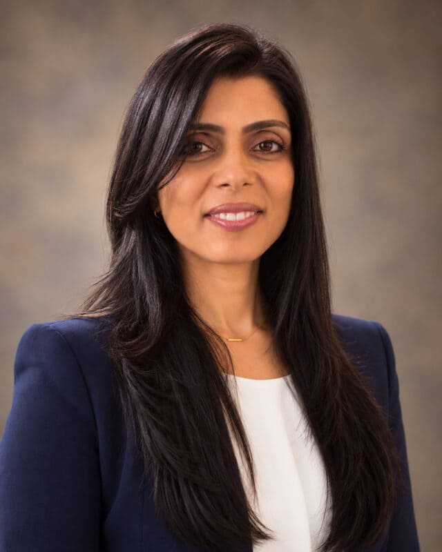 A woman with long dark hair wearing a navy blue blazer over a white top, smiling at the camera.