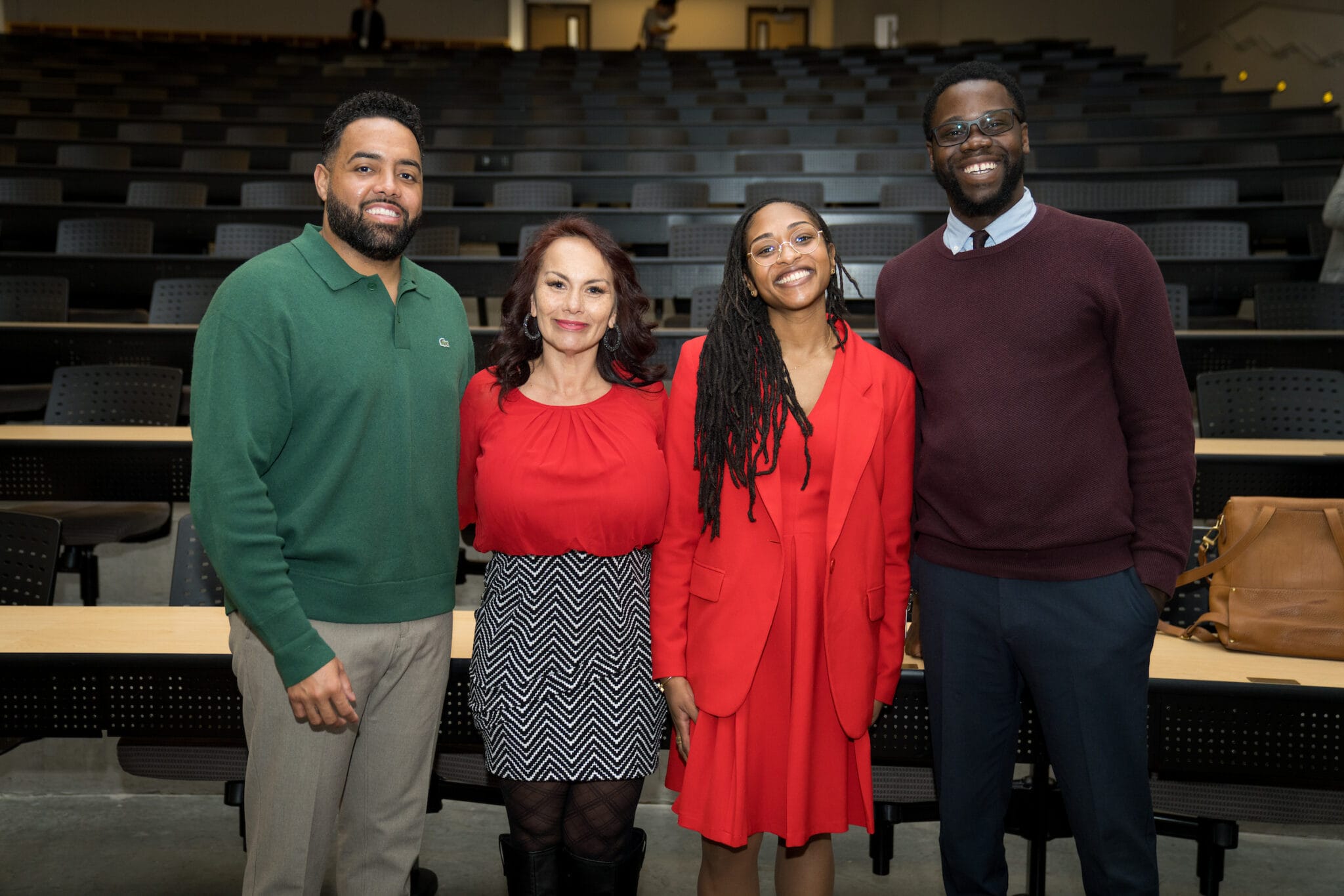 Four people stand smiling in the foreground of a lecture hall with empty rows of seats behind them.