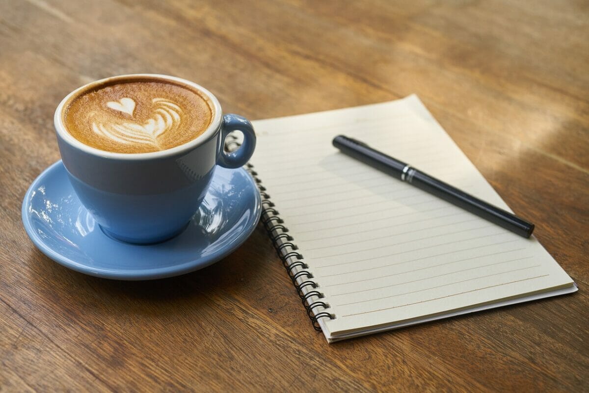 A cup of coffee with a notepad and pen on a wooden table.