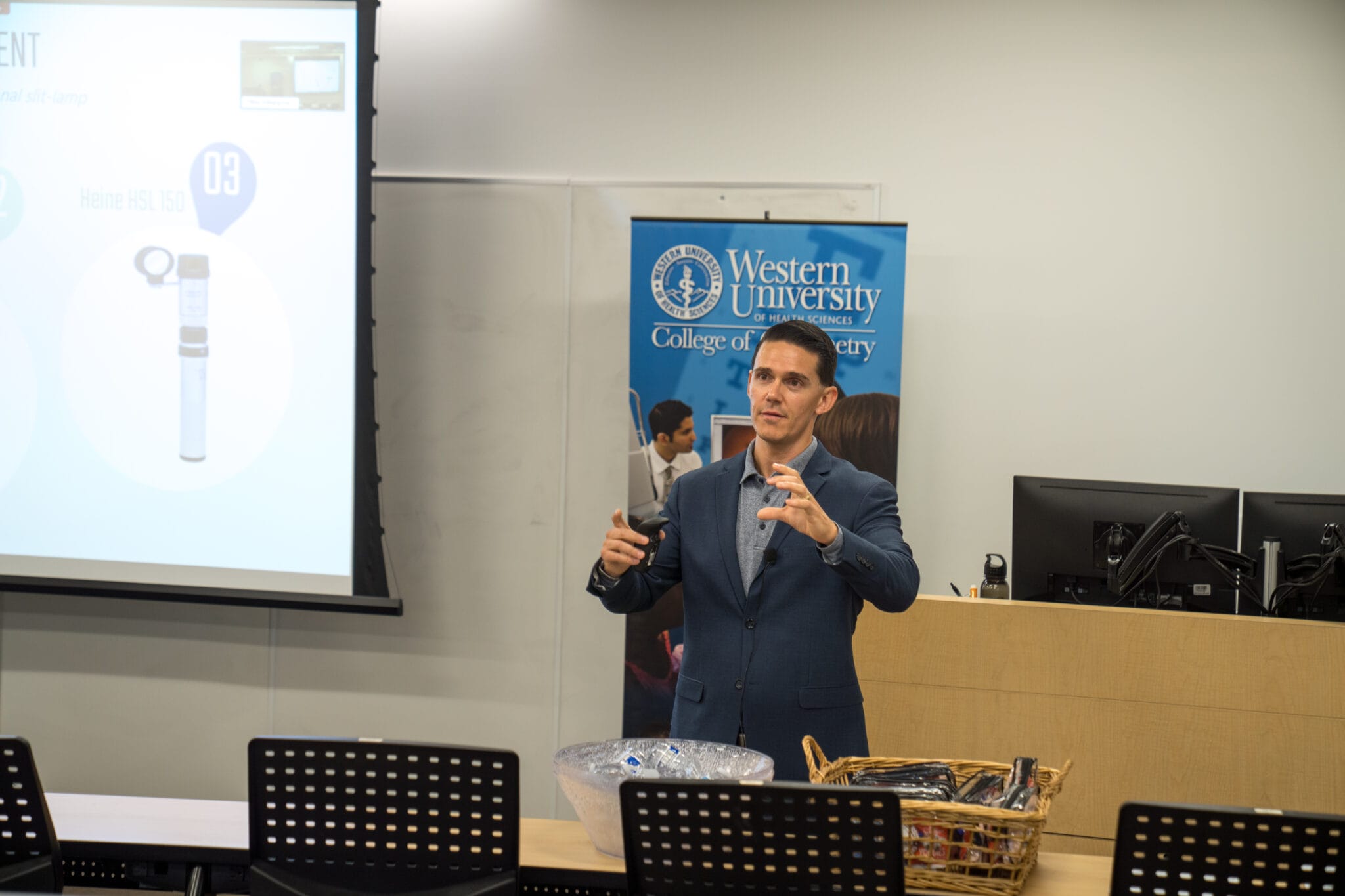 A man in a suit gives a presentation in a lecture hall with a Western University banner and a projected slide in the background.