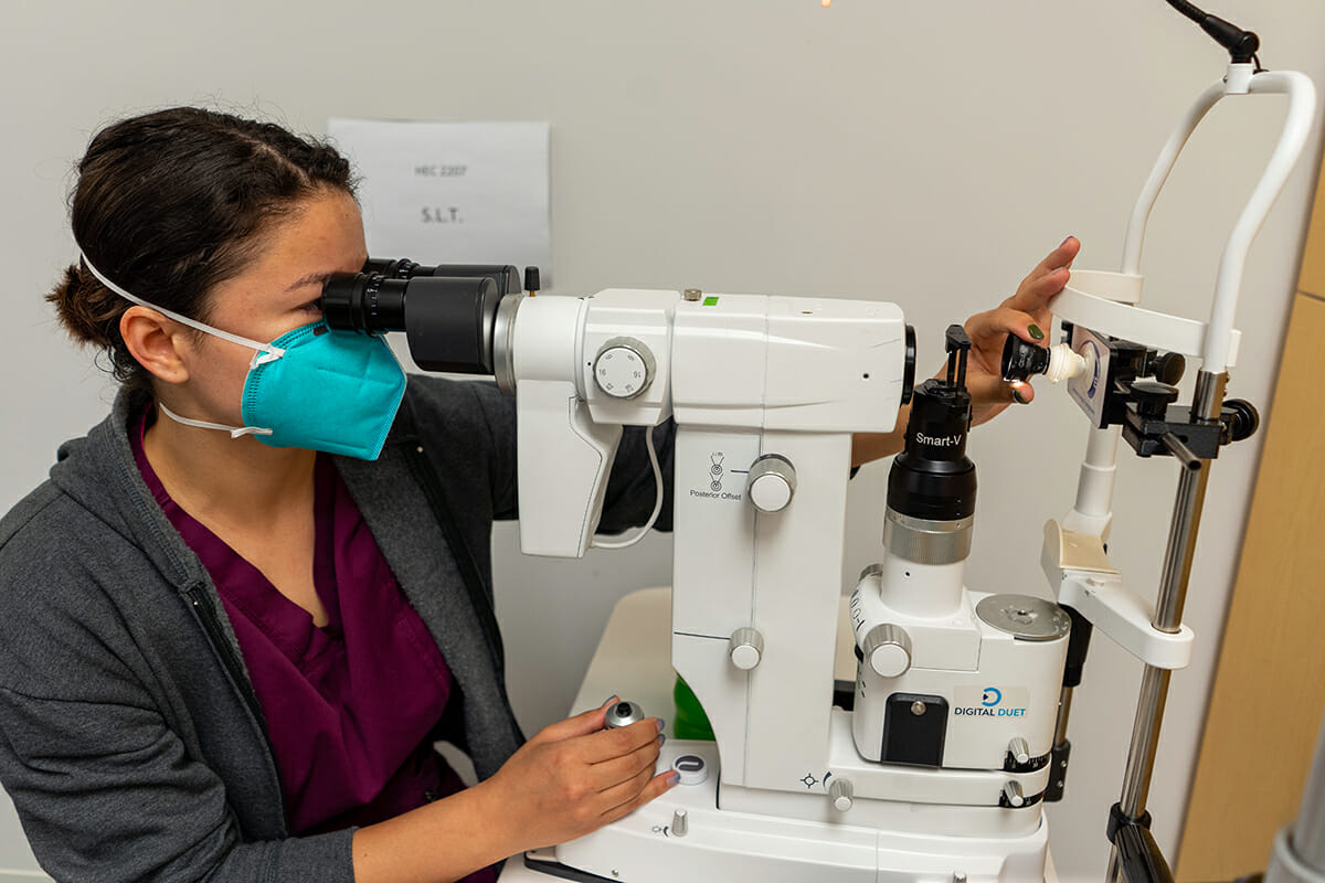 Student wearing face mask peering into optometry laser