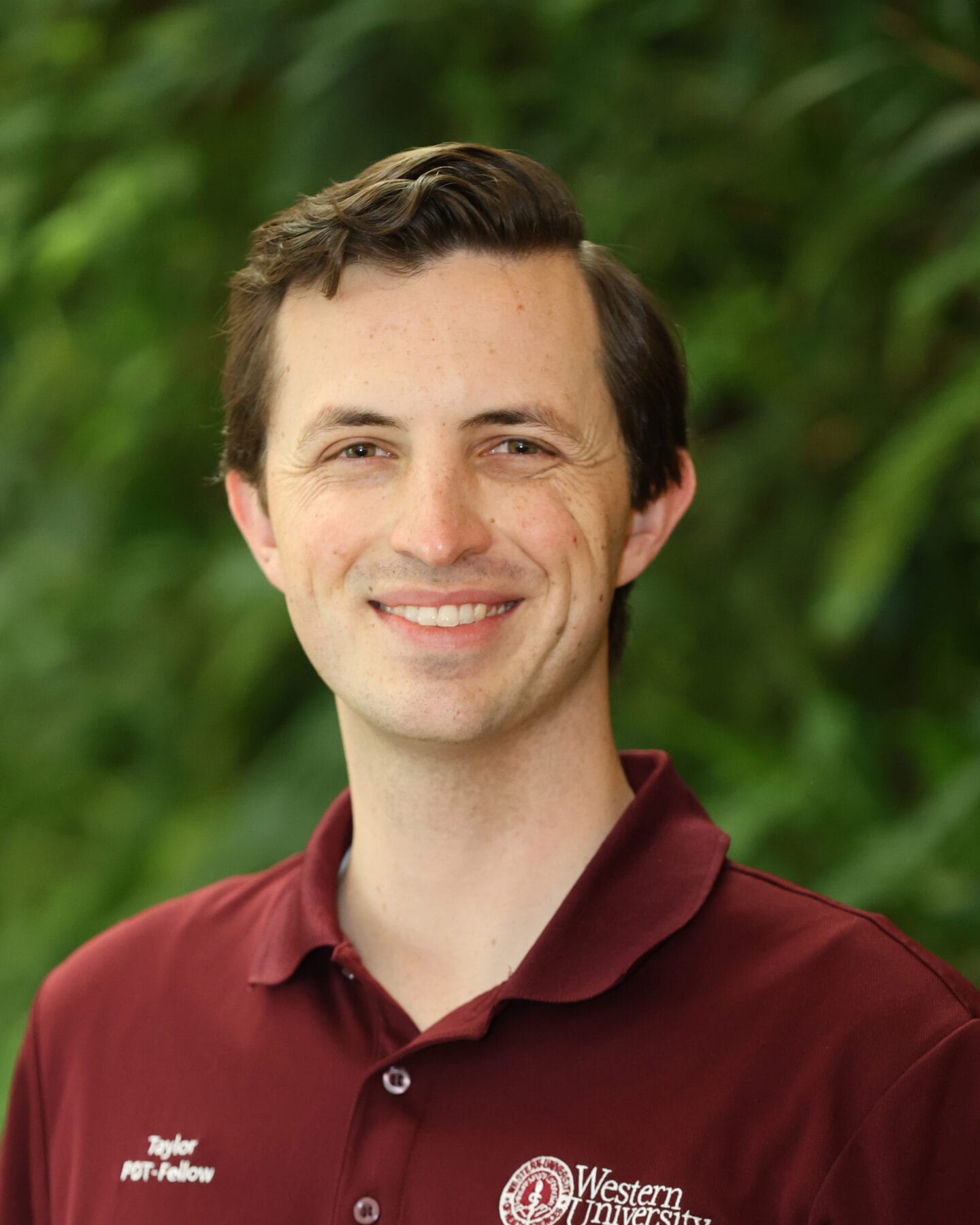 A person with short brown hair wearing a maroon Western University polo shirt smiles at the camera, with a blurred green background.