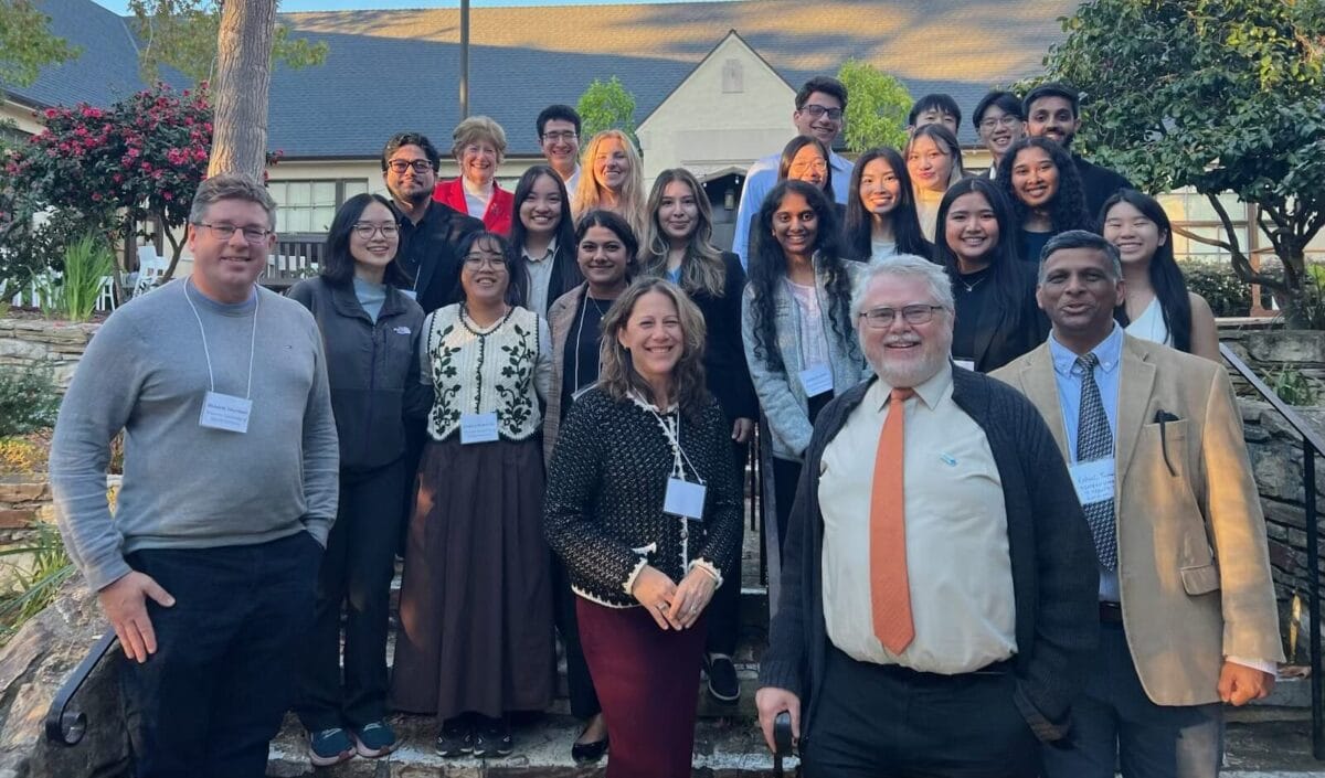 A group of adults and students, dressed in business casual attire with name tags, stand together outdoors on stone steps, posing for a group photo.