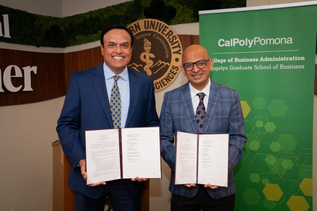 Two men in suits stand side by side holding open documents, posing for a photo in front of a Cal Poly Pomona banner and a Western University of Health Sciences sign.