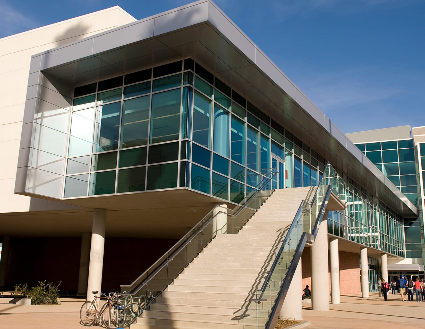 A modern building with large glass windows and an exterior staircase leading to the second floor; two bicycles are parked nearby.