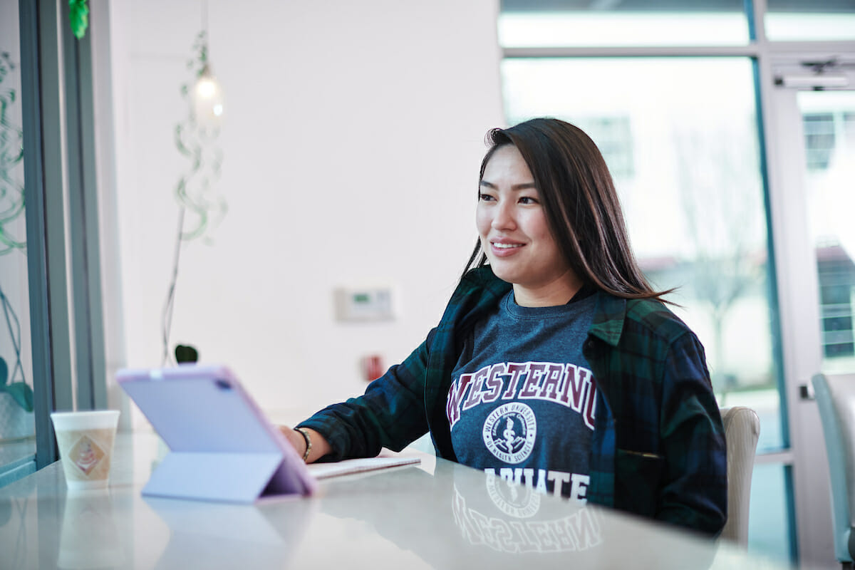 WesternU student sitting at a table using a laptop computer.