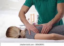 A person lying face down receives a back massage from a therapist in a clinic setting.
