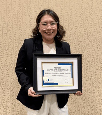A woman wearing glasses and a black blazer holds a framed award that reads, "ASOA 2023 Chapter of the Year Award, Western University of Health Sciences College of Optometry.