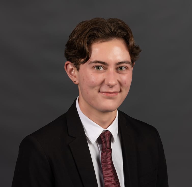 Young person in a suit and red tie poses for a formal portrait against a plain dark gray background.