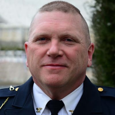 A middle-aged man in a police uniform stands outdoors, looking at the camera with a neutral expression.