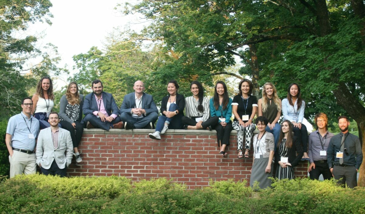 Students in a group photo, outdoors standing near and sitting on brick wall