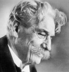 Older man with wavy grey hair, a large mustache, and a suit, looking downward in a black-and-white portrait.