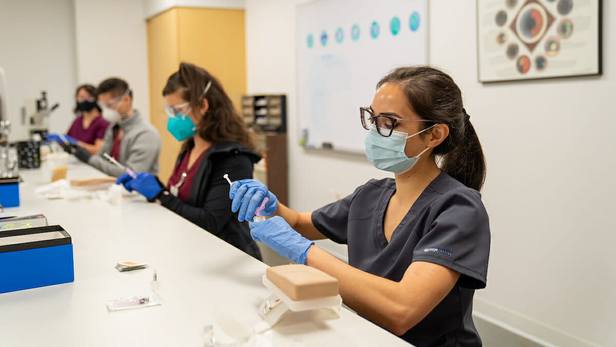 Third-year College of Dental Medicine student Chelsea Director upacks a needle. College of Graduate Nursing Professor and Associate Dean of Administration and Research Rodney Hicks, PhD, teaches a safe injections techniques workshop to College of Optometry and College of Dental Medicine students Wednesday, April 21, 2021. Following the workshop, the students administered vaccine shots for the first time at WesternU Health Vaccine Clinic.