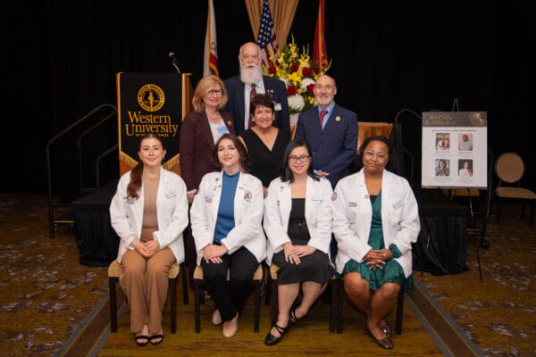 Eight people in a group photo, four standing in the back row, four sitting.
